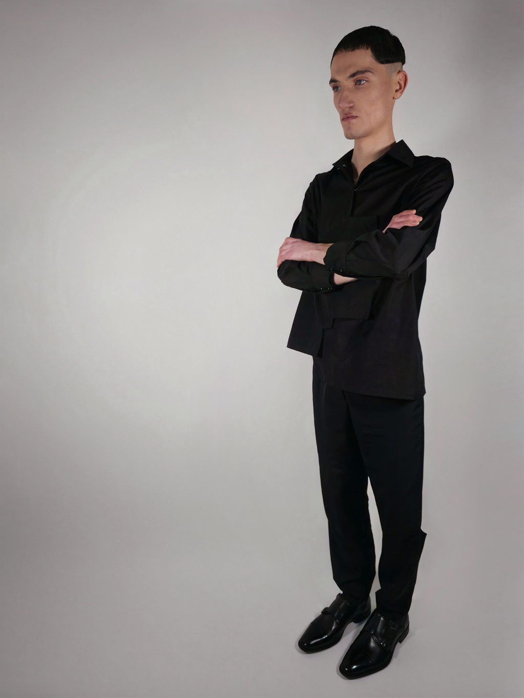 Vue de trois quarts d’un homme portant la chemise en coton Stephen, noire et asymétrique, avec le pantalon Stéphane.