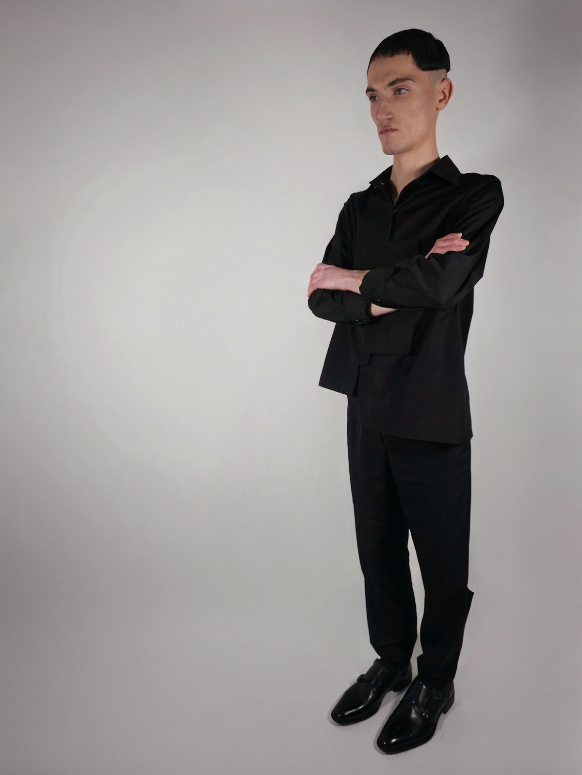 Vue de trois quarts d’un homme portant la chemise en coton Stephen, noire et asymétrique, avec le pantalon Stéphane.