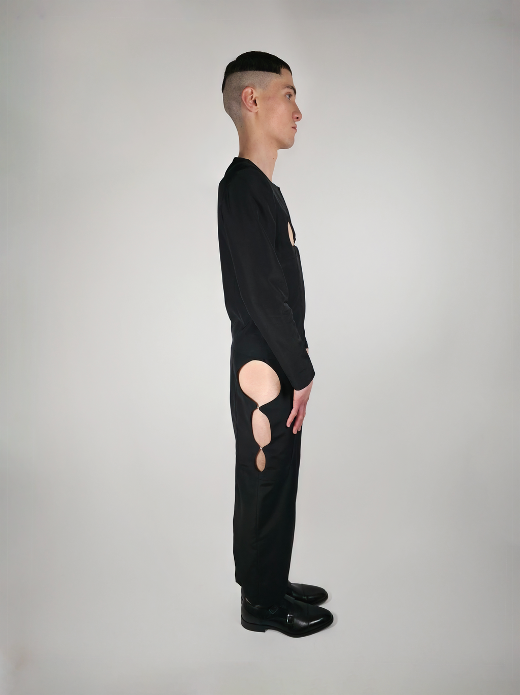 Vue de côté de la jupe longue crayon noire Théphaline portée par un homme, avec une ouverture sur le côté dévoilant la jambe, portée avec la veste Tyffaine.