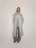 Femme portant le manteau long Michelle gris, fermé en haut, avec son grand col rabattu. Porté avec le pantalon Michael et la robe Myshellie.