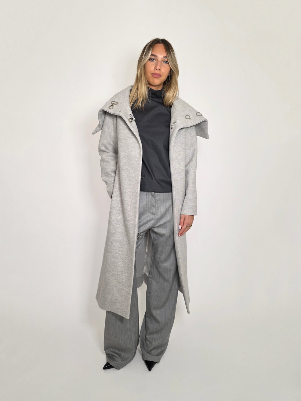 Femme portant le long manteau Michelle gris en laine avec le haut gris Mitchel et le pantalon gris Michael.